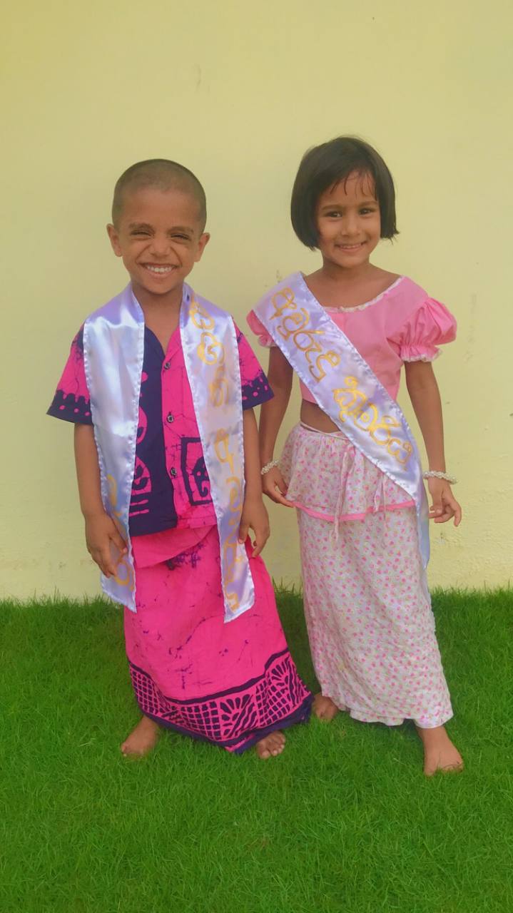 Children in vibrant traditional attire smiling barefoot on a grassy lawn.