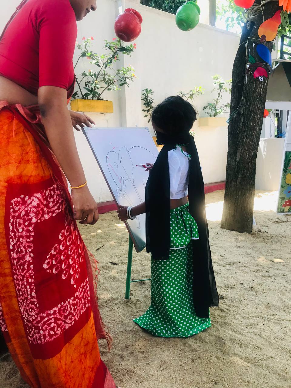 Outdoor educational activity with teacher and student, surrounded by festive decorations and greenery.