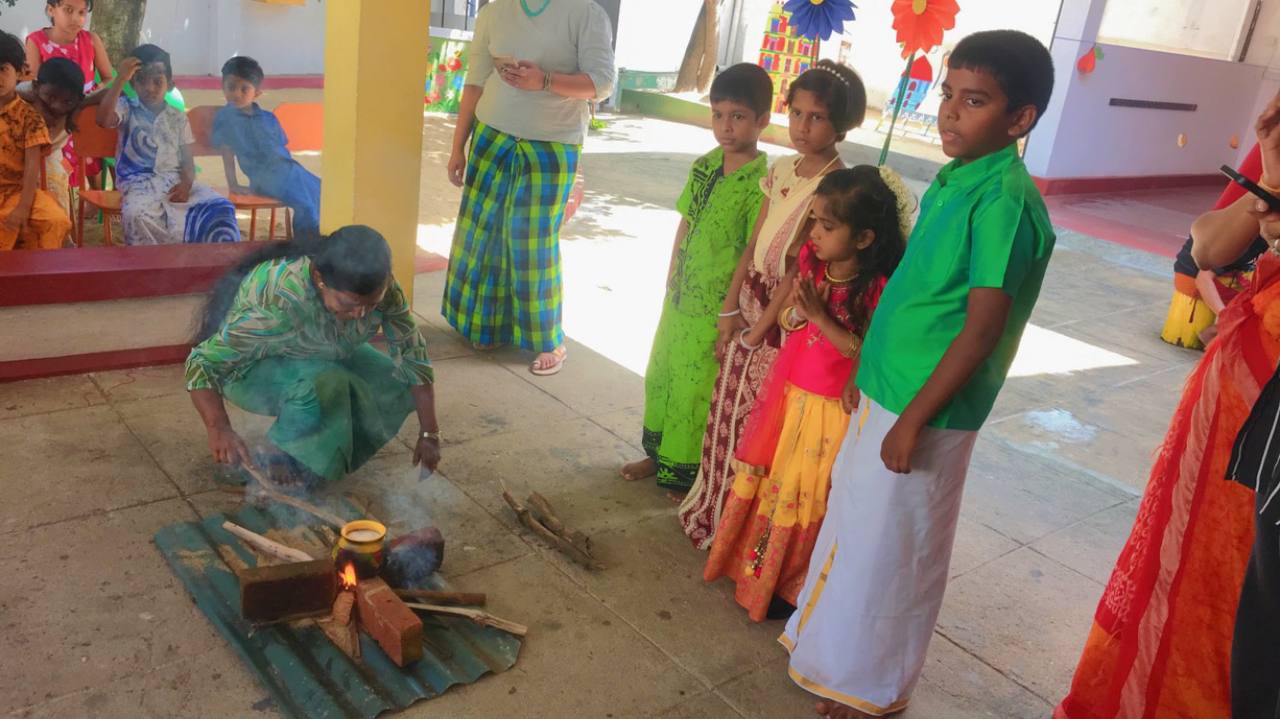 Woman tending ritual fire as children observe in traditional attire.