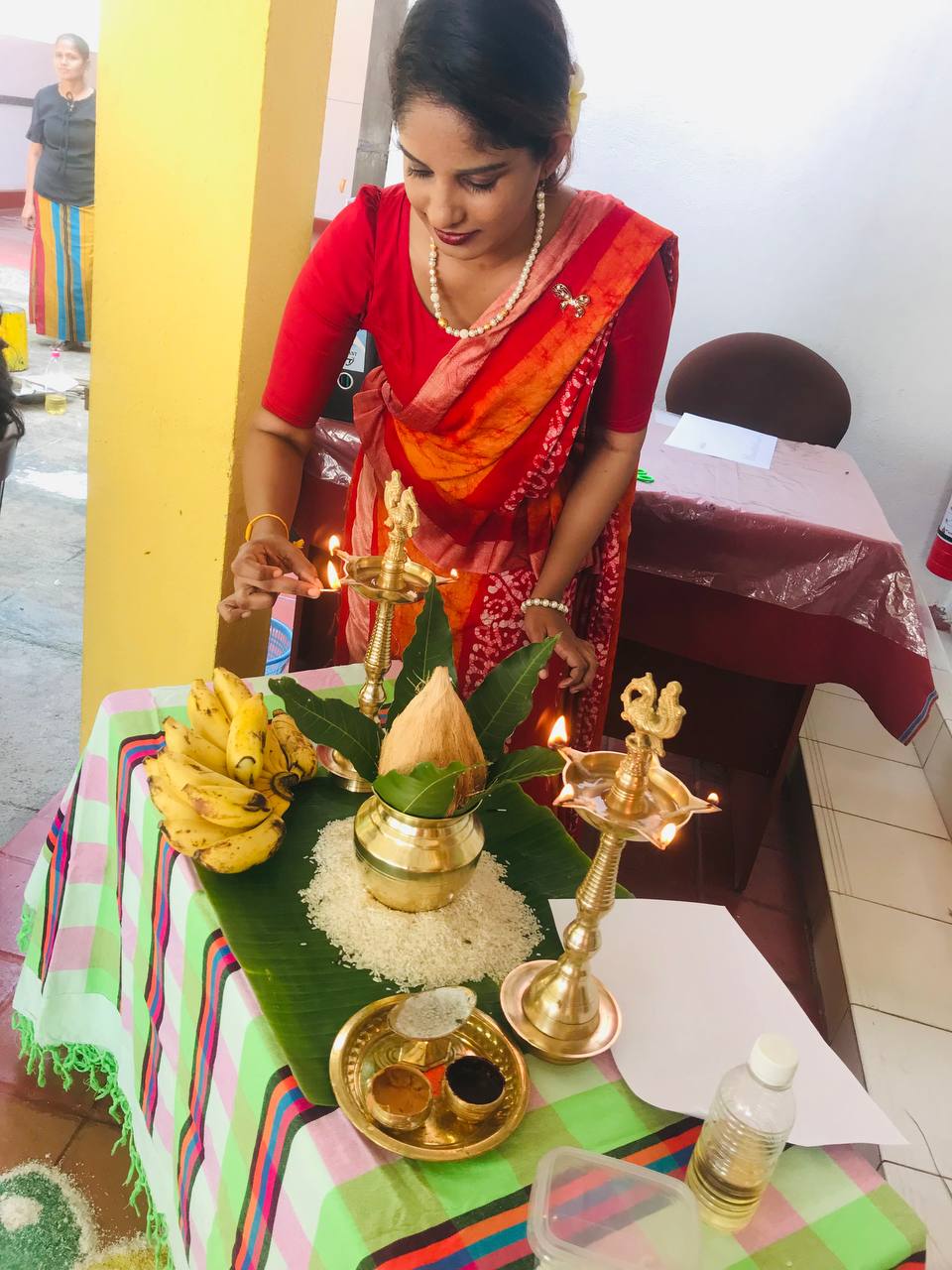 Woman in red saree lighting brass lamp on decorated ritual table indoors.
