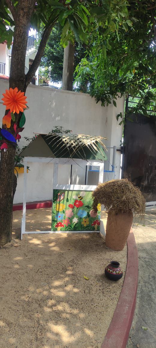 Garden with decorated tree, colorful flowers, rustic pots, and a bamboo-roofed structure.