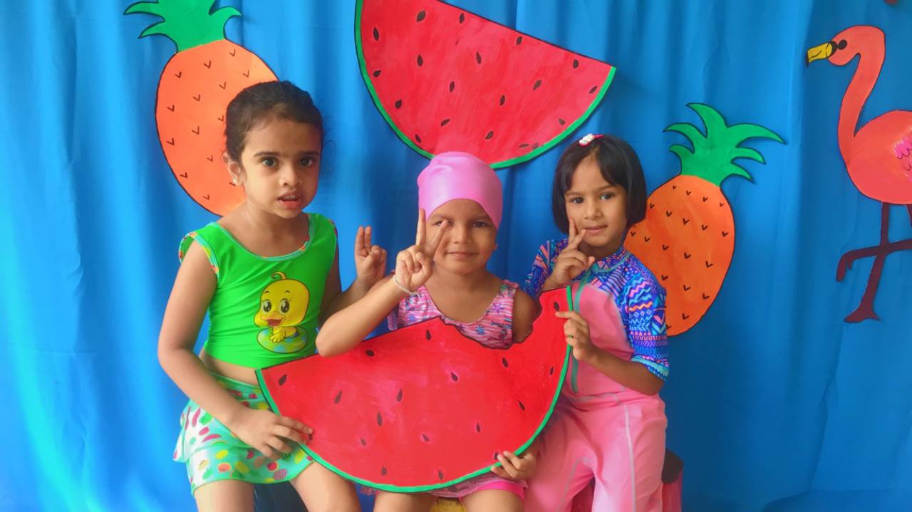 Three happy children in colorful outfits posing with tropical decorations.