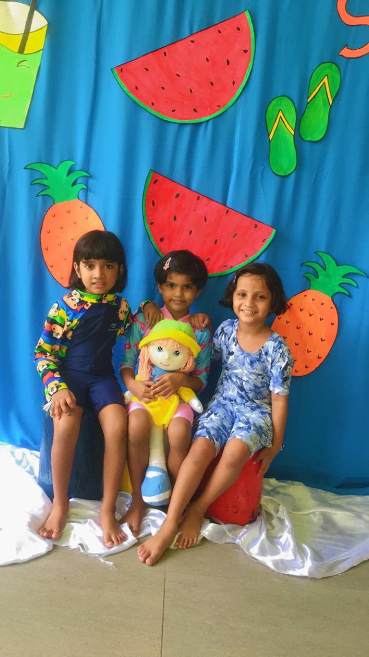 Three happy kids in summer-themed outfits with watermelon and pineapple decorations.