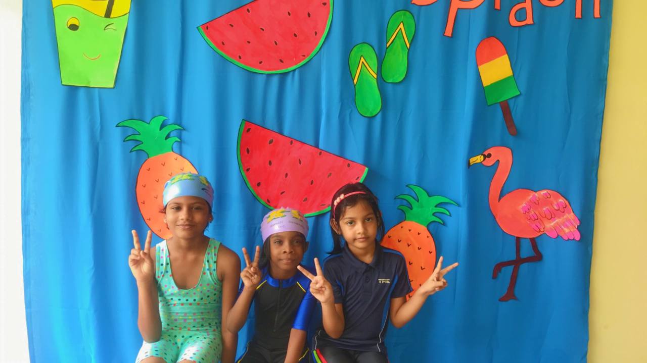 Three children posing joyfully in front of a colorful summer-themed backdrop.