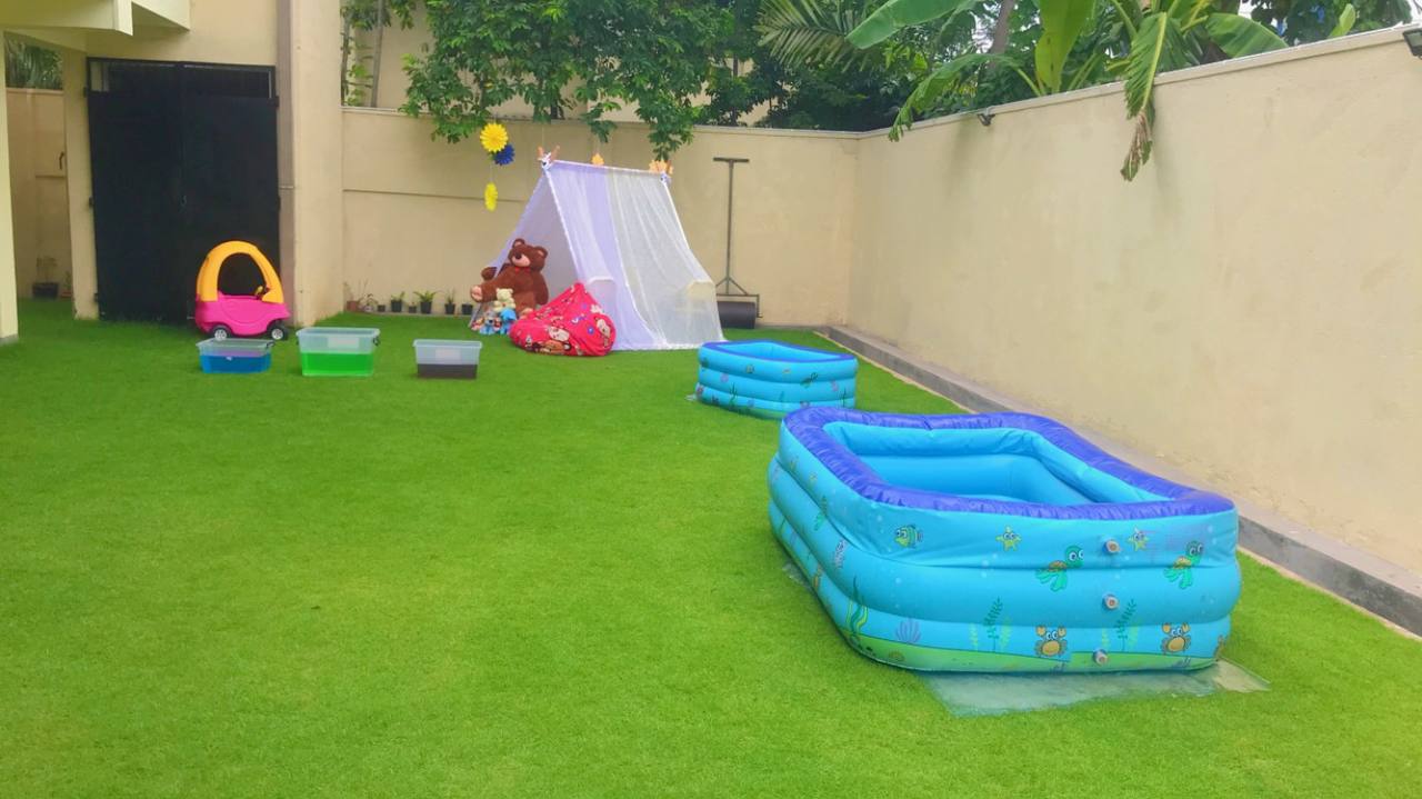 Family yard with inflatable pools, play tent, and childrens toys on green grass.