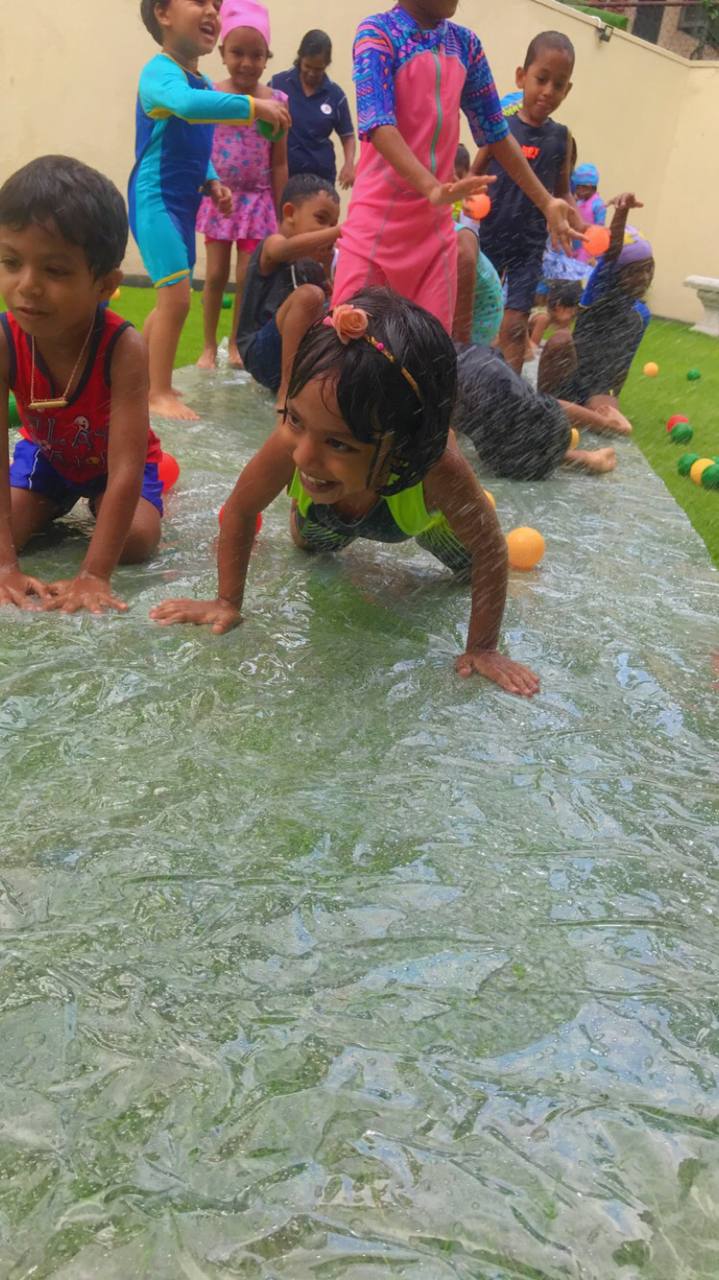 Kids playing joyfully on slip-and-slide in colorful swimsuits.