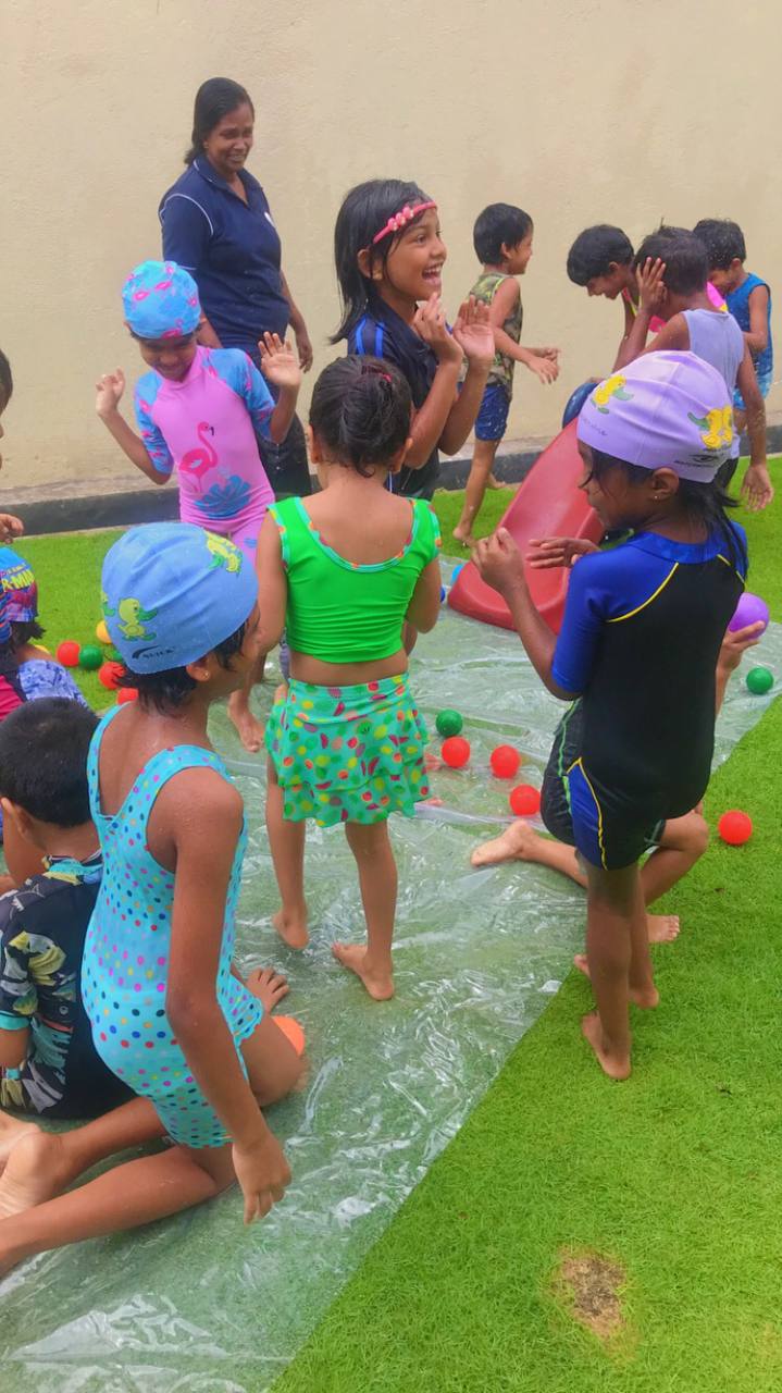 Children playing on slip-and-slide with colorful balls; supervised water fun outdoors.