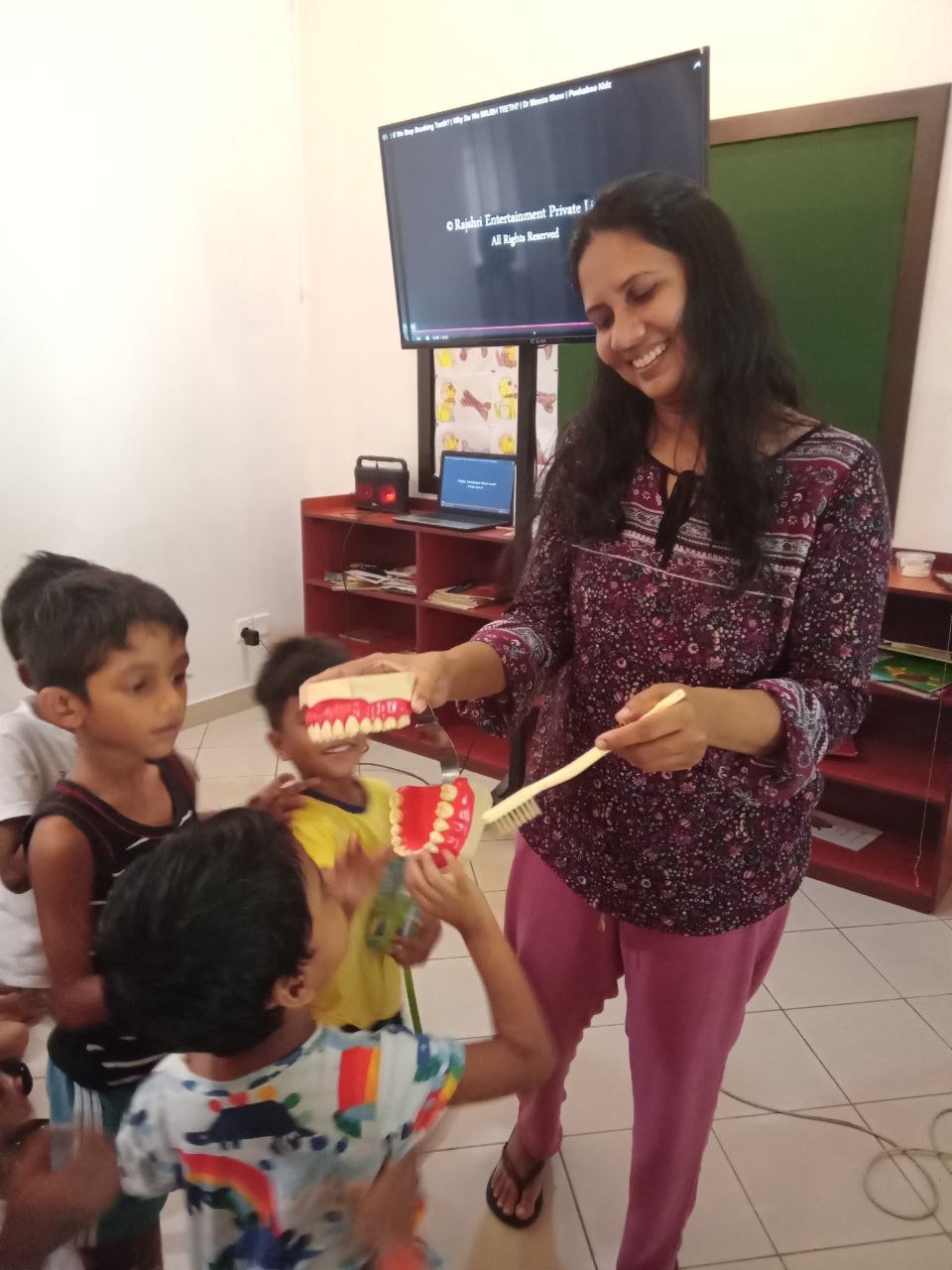 Woman teaching kids dental hygiene with a large model and giant toothbrush.