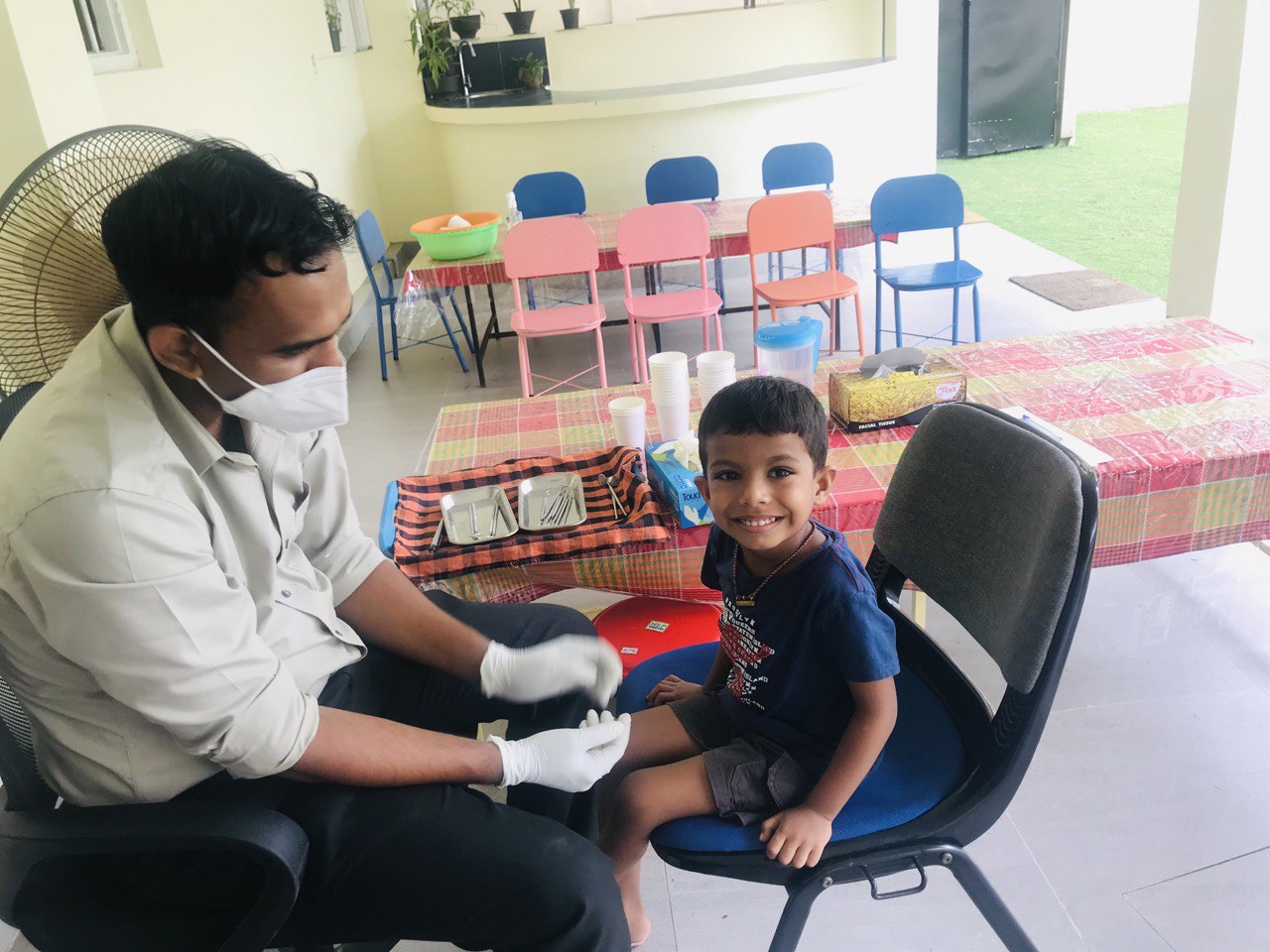 Child receiving a health check-up from a masked professional in a colorful room.