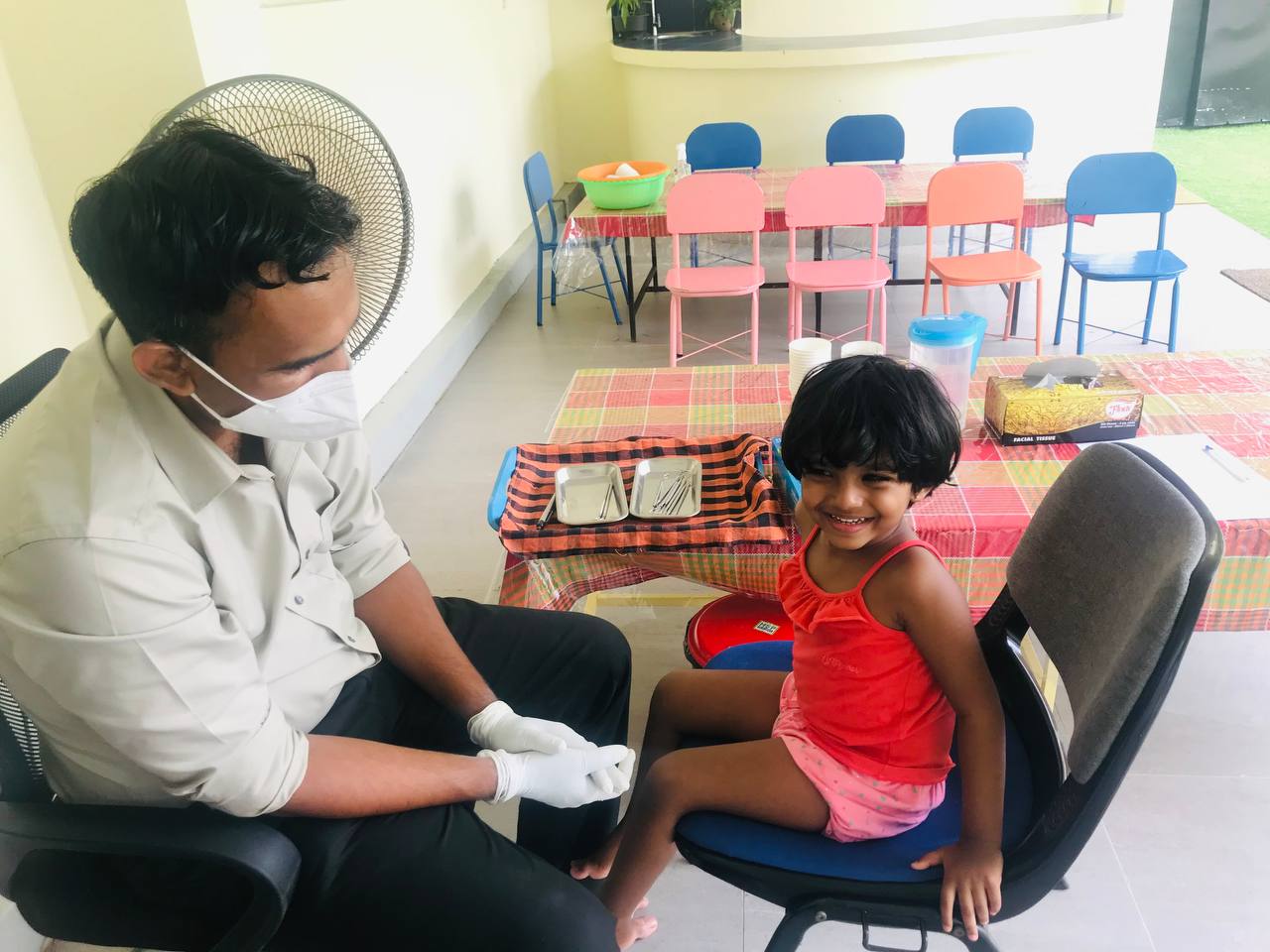 Smiling girl in red top at pediatric checkup with caring medical professional.