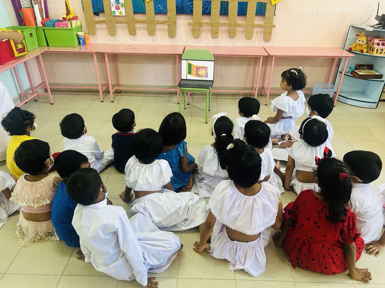 Children in traditional attire watching a screen in a bright, educational classroom.