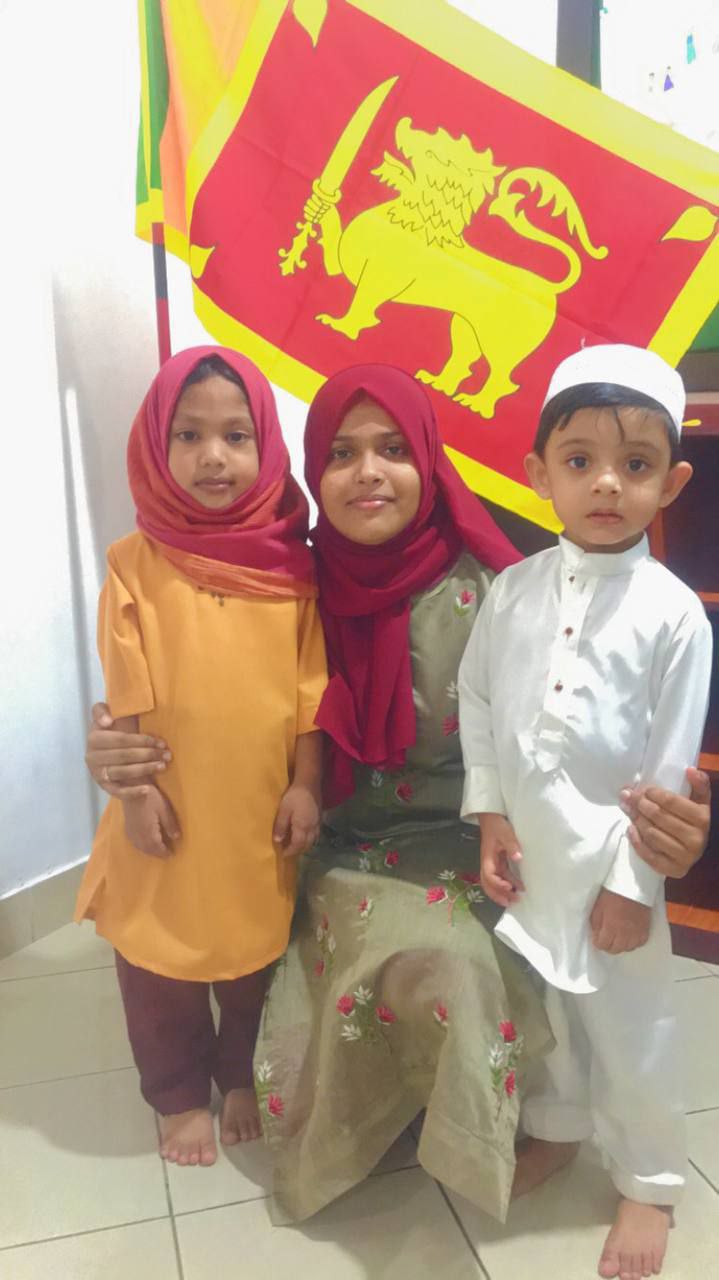 Sri Lankan family smiling in traditional attire in front of their national flag.