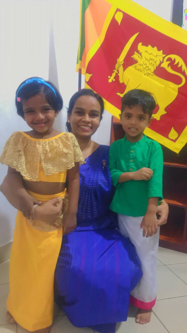 Mother and children in colorful attire celebrating Sri Lankan heritage indoors.
