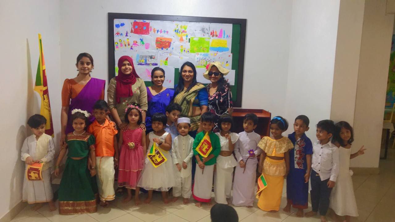 Adults and children in traditional attire at a cultural celebration with colorful artwork displayed.
