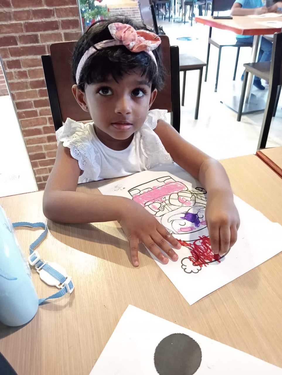 Young girl coloring at café table with natural light.