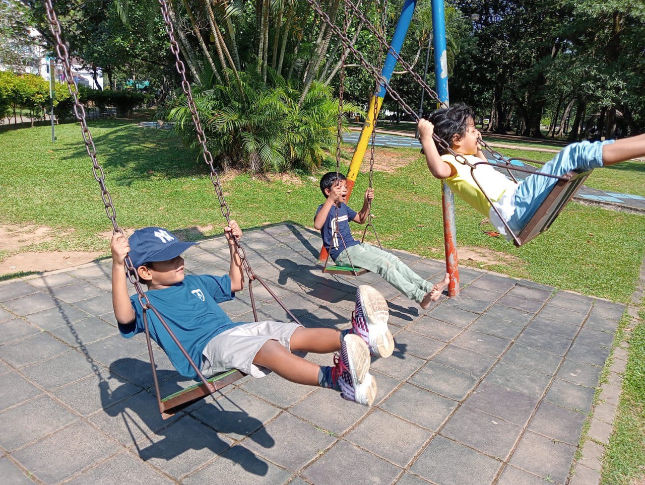 Children swinging joyfully in a colorful park on a sunny day.