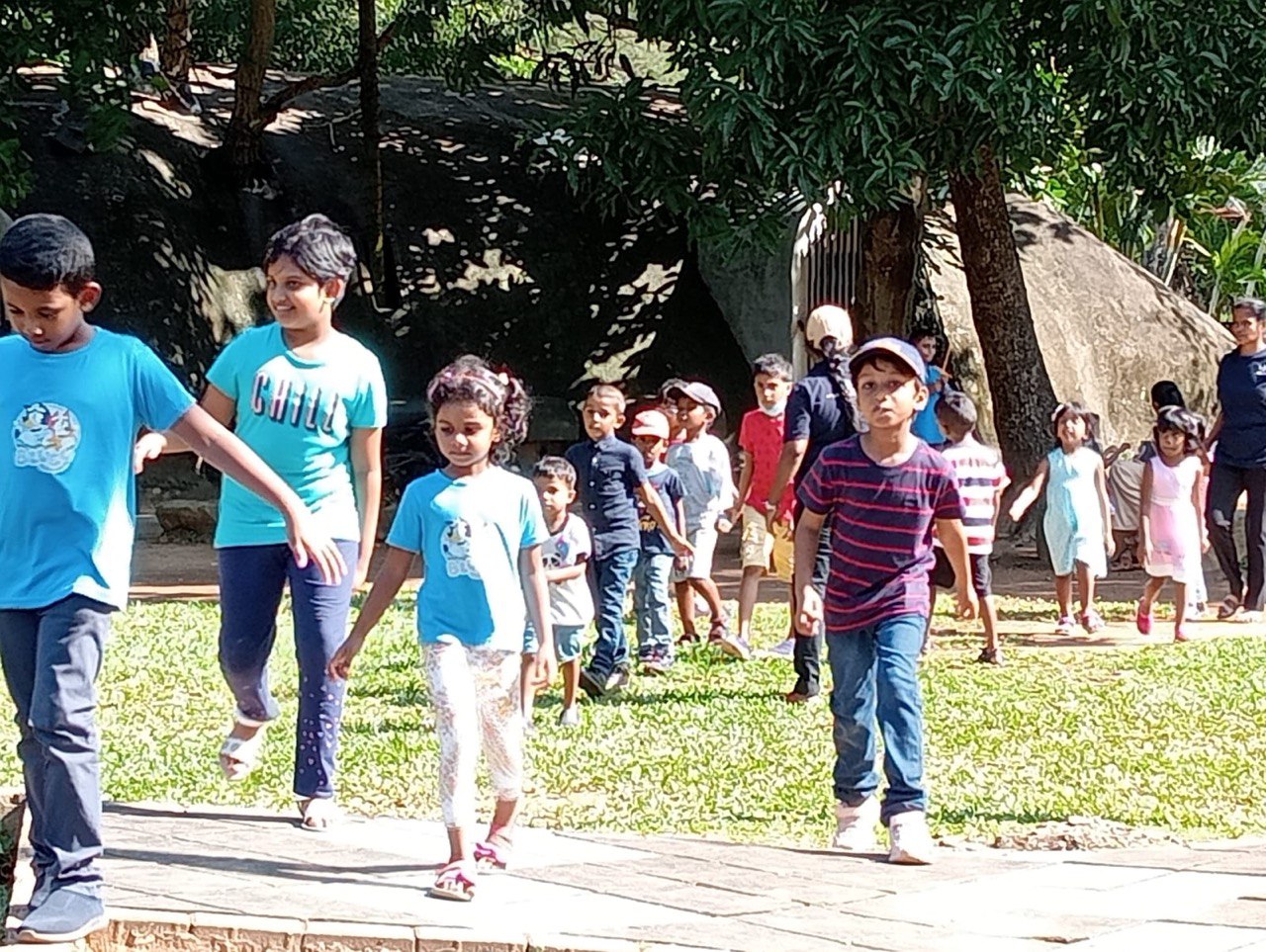Children walking in a park on a sunny day, dressed in casual clothing.