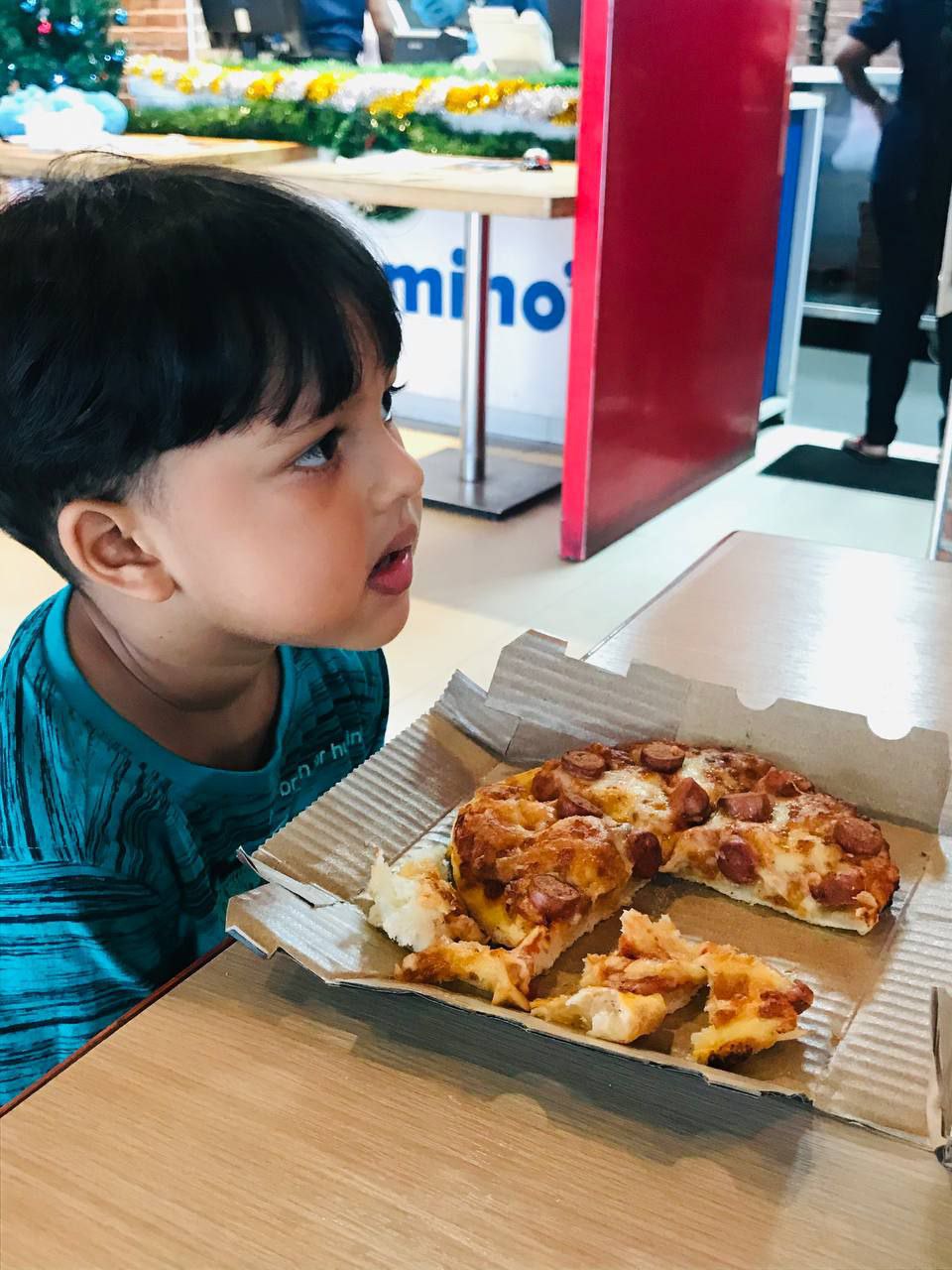 Child enjoying pizza at Dominos restaurant with festive decor in the background.