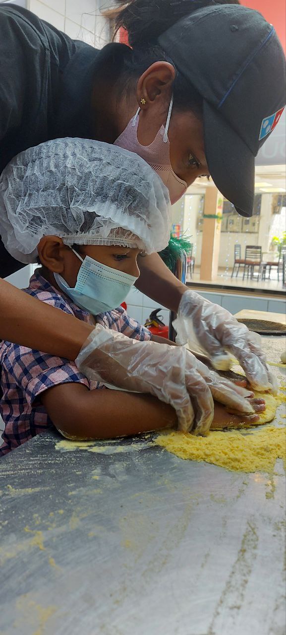 Adult helping child cook in a sanitized kitchen setting. Both wear masks and gloves.