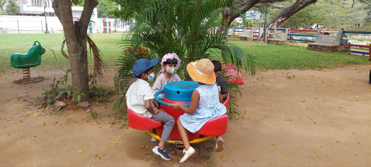Children playing on a colorful merry-go-round in a sunny outdoor park.