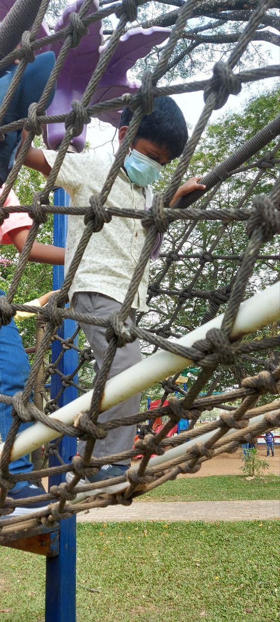 Child in face mask climbing rope structure at sunny playground.