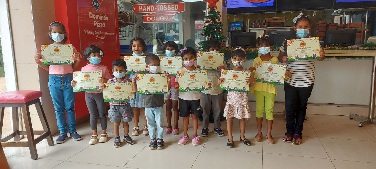 Children holding certificates in a festive community center during a holiday awards ceremony.