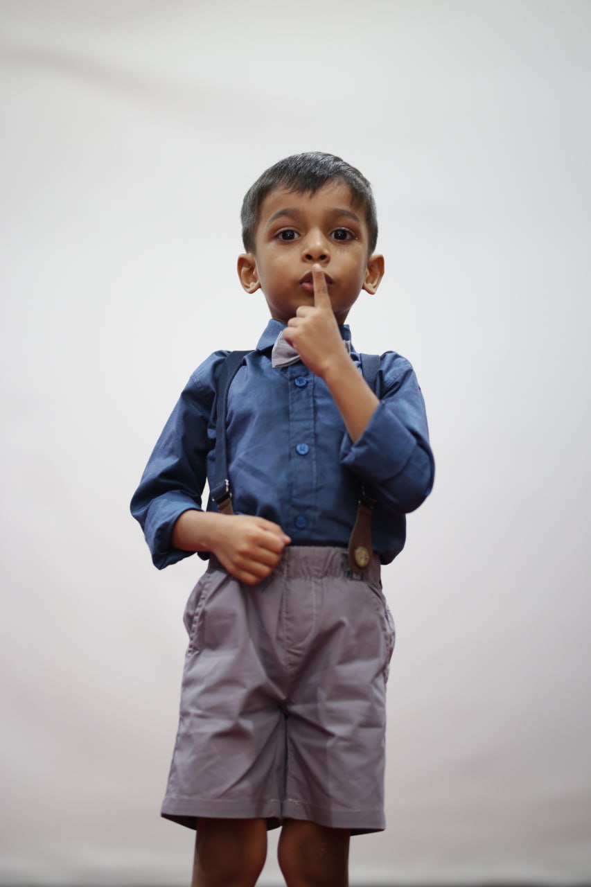 Curious boy in blue shirt and suspenders, finger on lips, thinking.