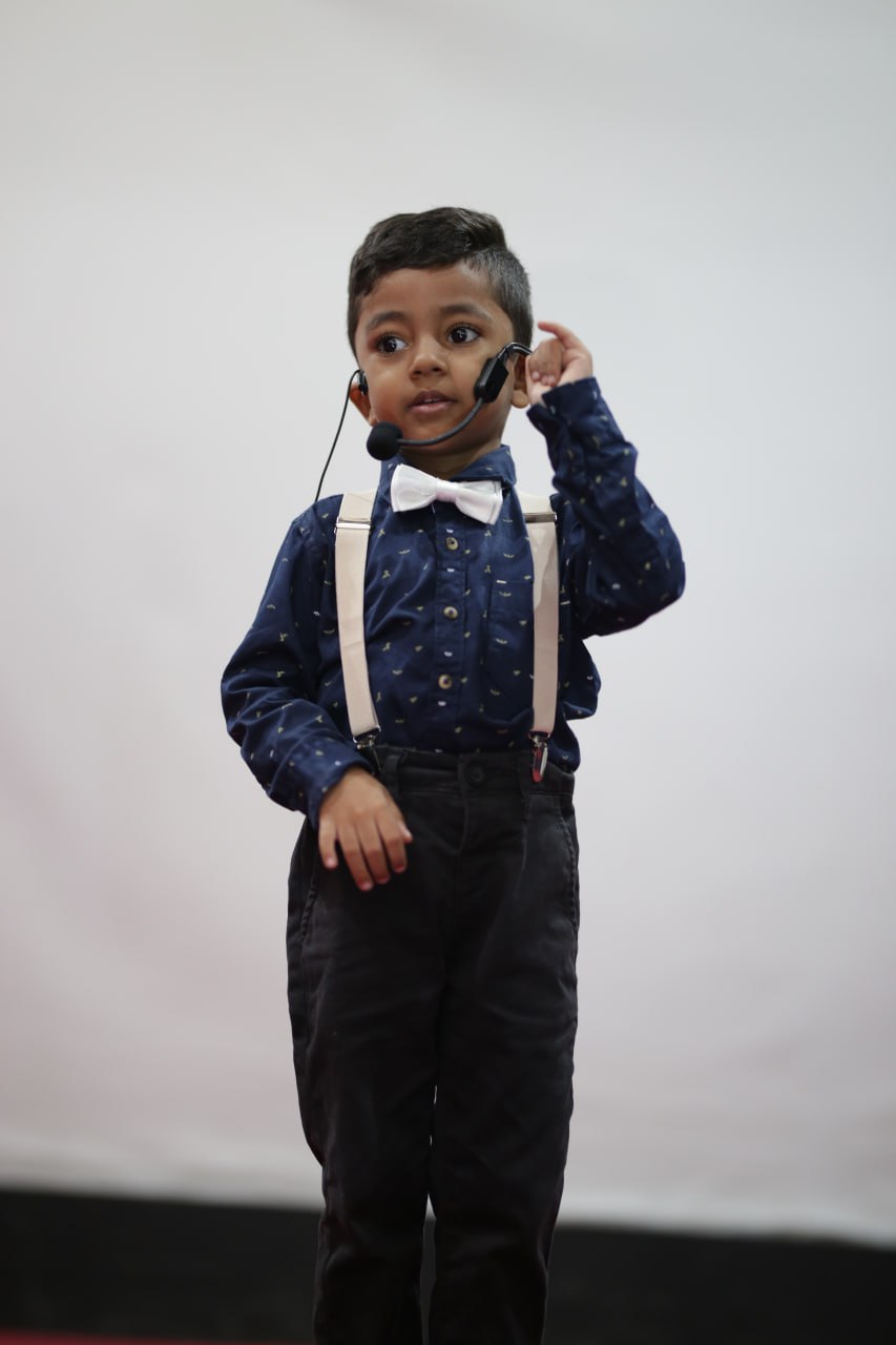 Young boy in formal attire speaking with a headset microphone on stage.