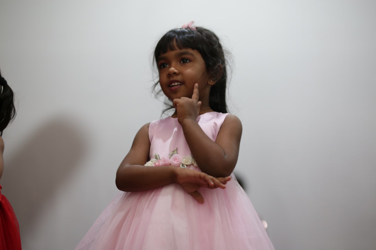 Young girl in pink tulle dress, finger on chin, thoughtful pose.