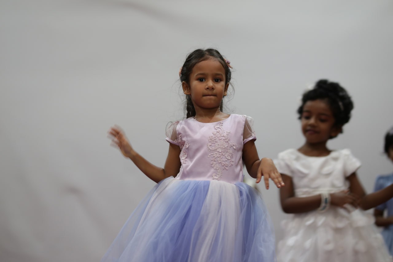 Young girls in pastel dresses performing at an indoor event.