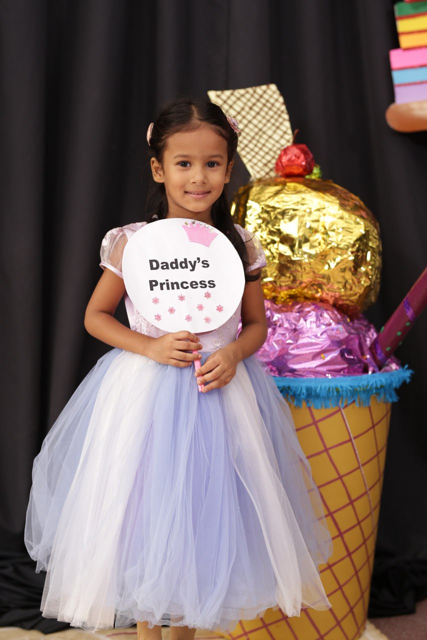 Young girl in a pastel dress holding Daddys Princess sign with whimsical ice cream backdrop.