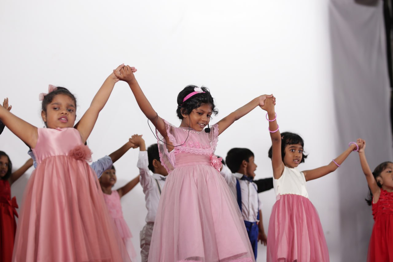Children in pink and white dresses joyfully performing a choreographed dance.