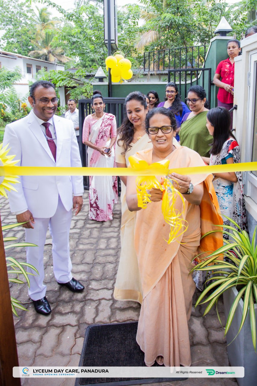 Elderly woman cuts ribbon at grand opening, surrounded by smiling attendees in colorful traditional attire.