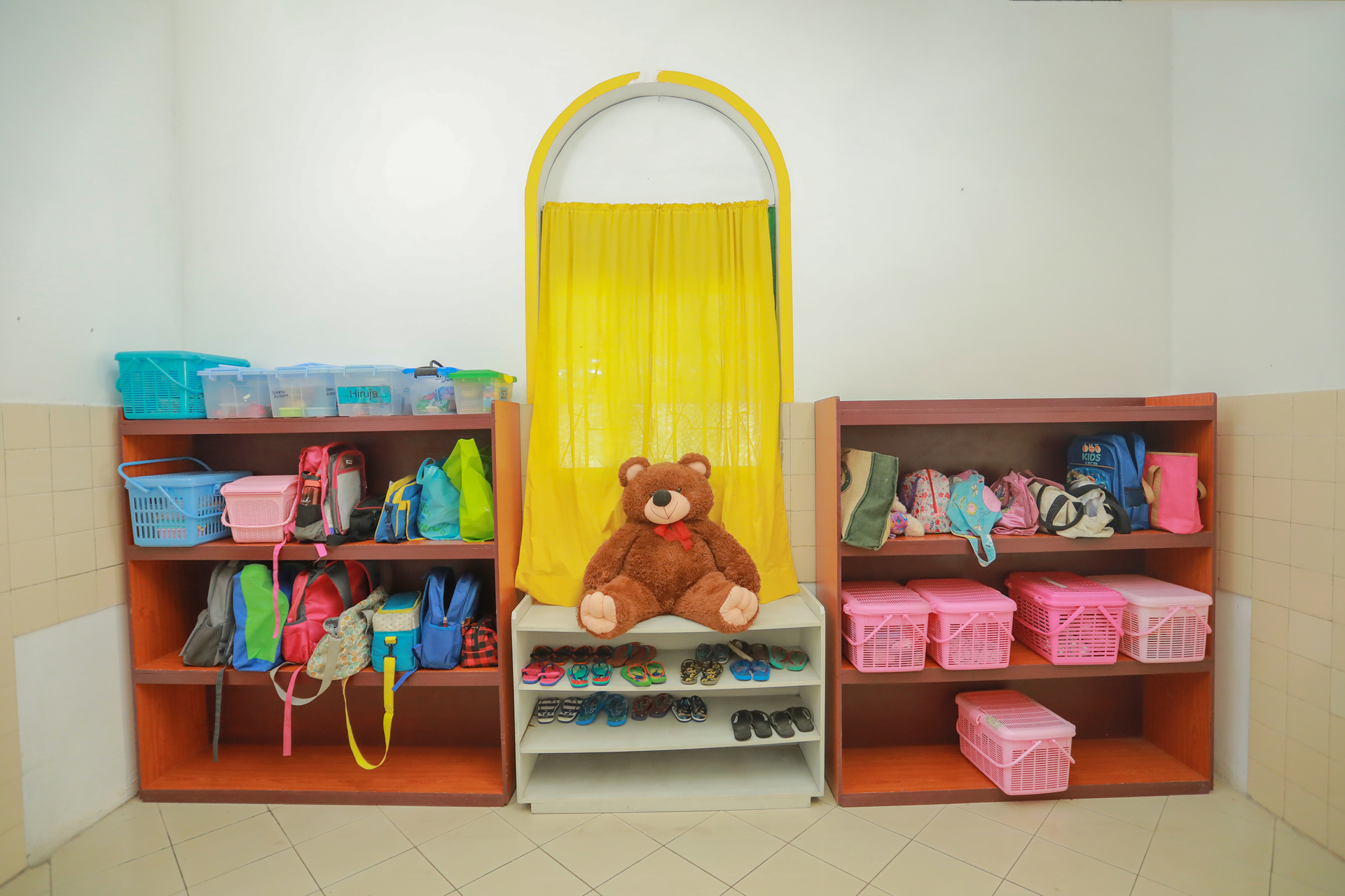 Organized childrens storage area with colorful bins, bags, and a central teddy bear.