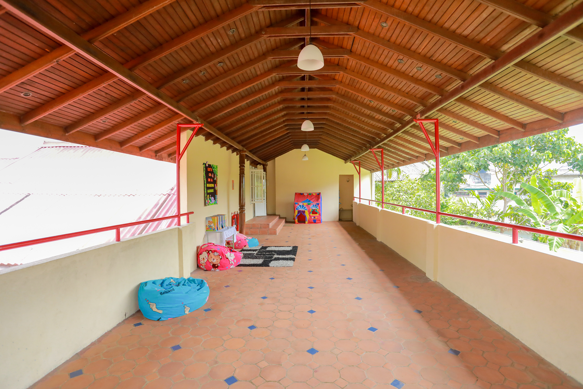 Colorful corridor with bean bags, wooden ceiling, and views of lush greenery.