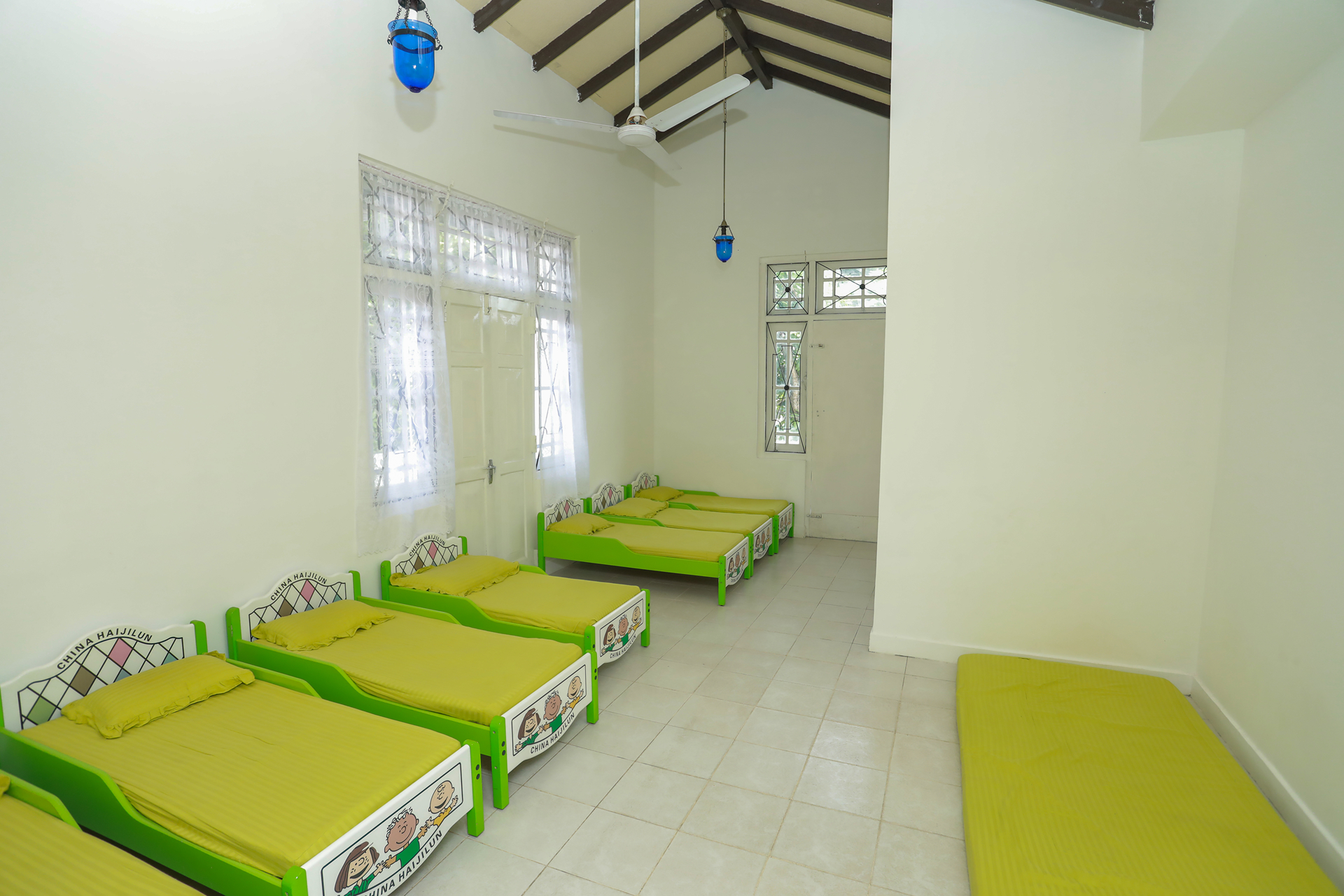 Bright dorm room with green beds, natural light, and exposed wooden beams.