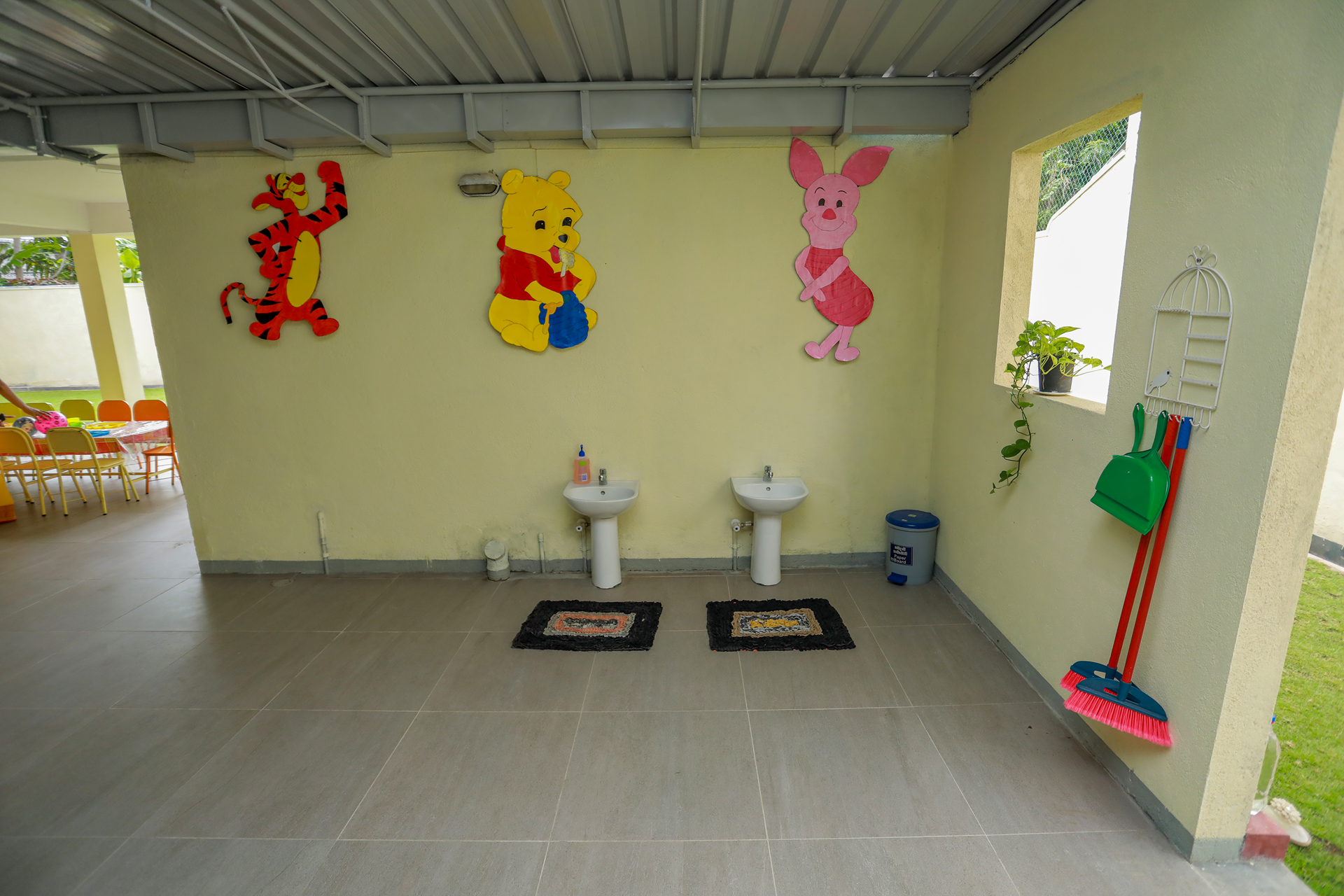 Bright childrens washroom with cartoon decals, small sinks, colorful chairs, and cleaning tools.