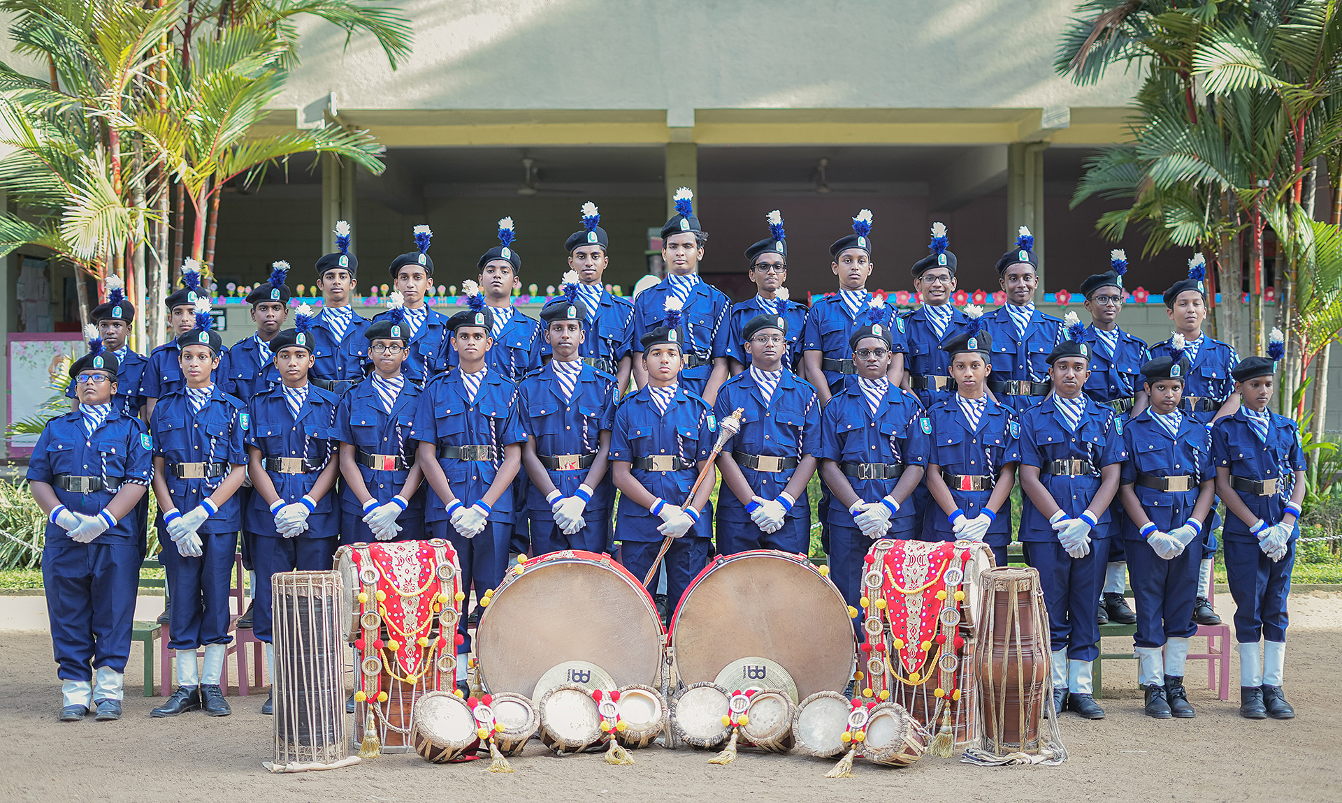 Group of cadets in blue uniforms with traditional drums outside a school building.