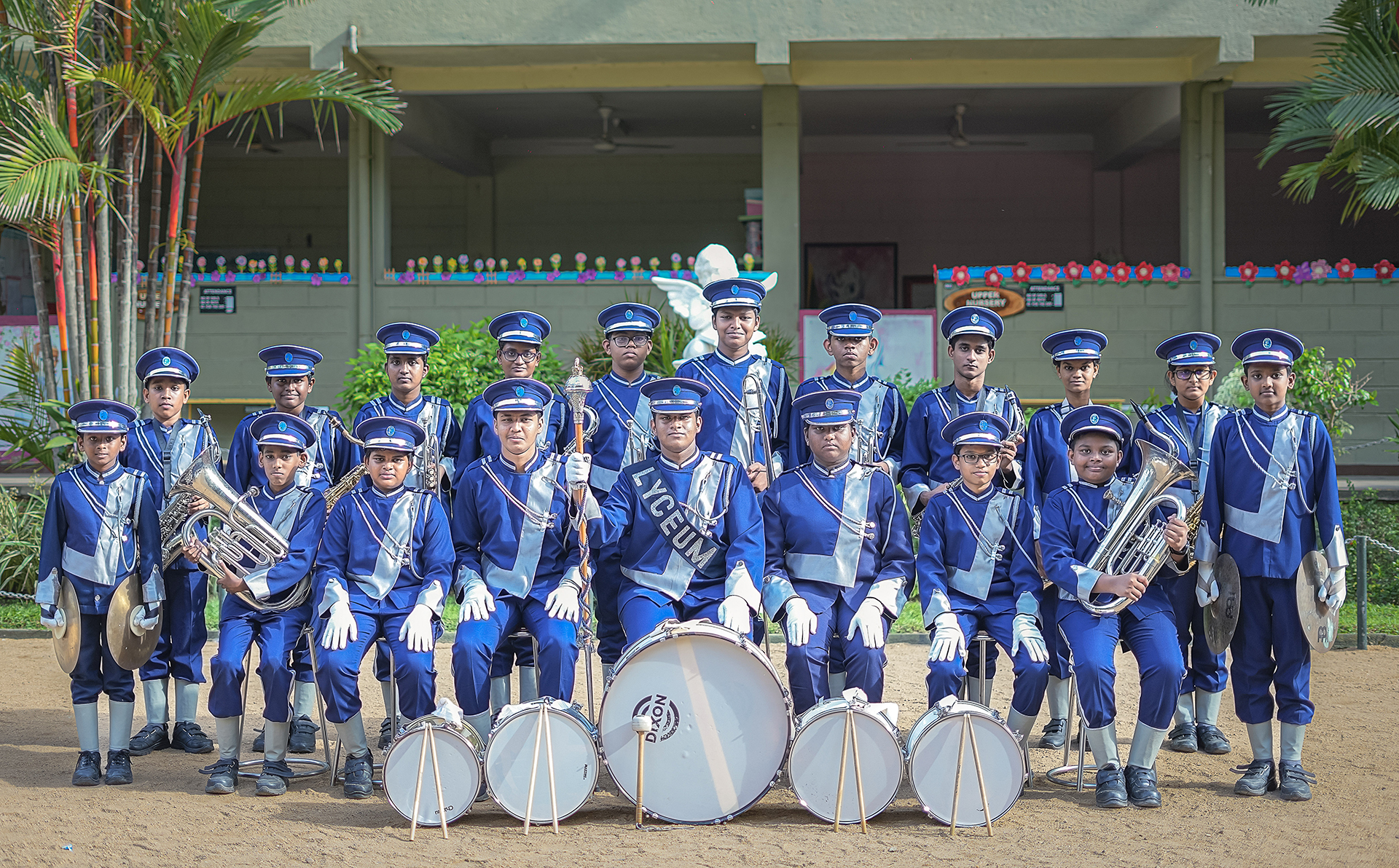 Marching band in blue uniforms posing with instruments outside a festively decorated building.