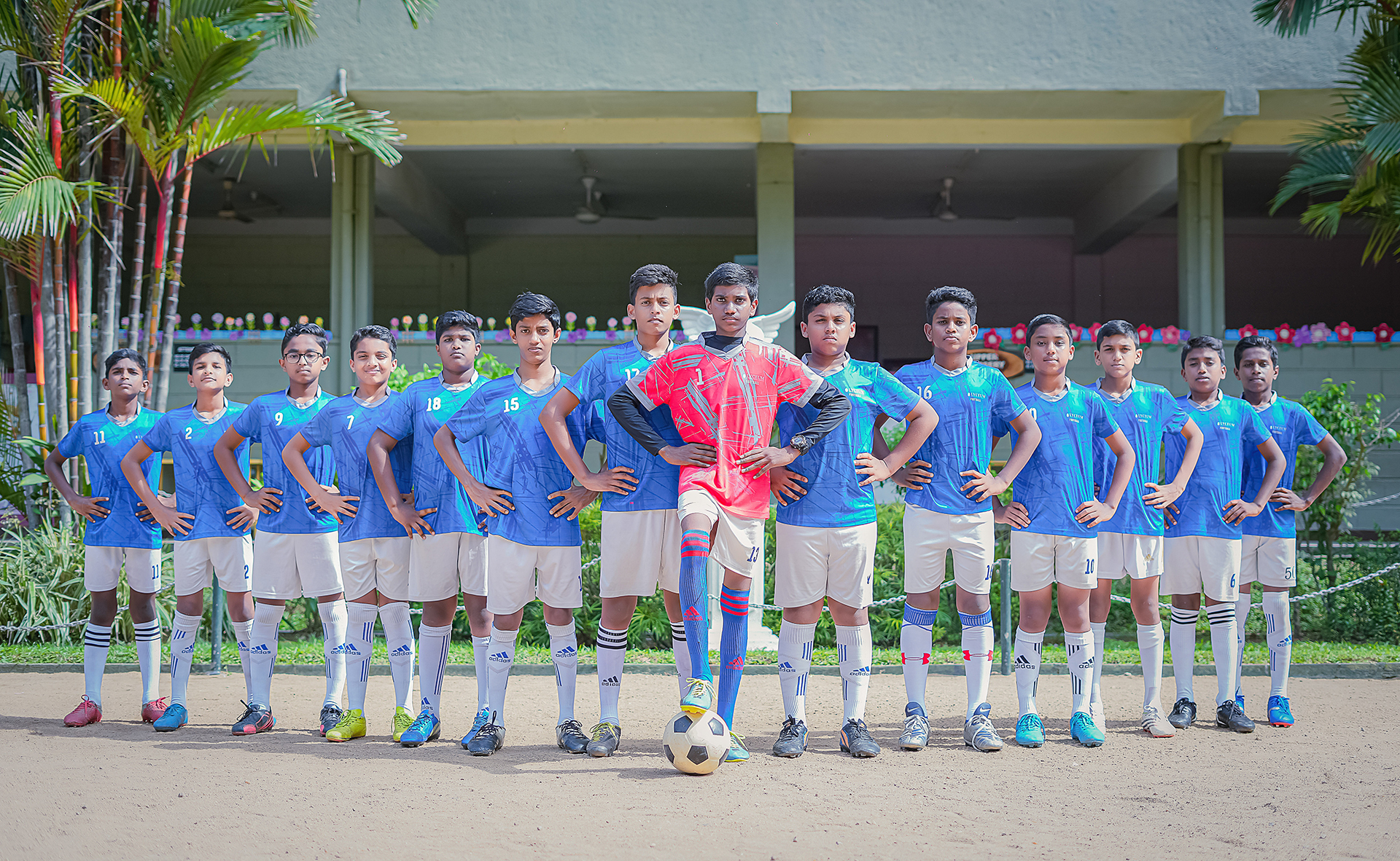 Youth soccer team in blue uniforms with red-jerseyed goalie, standing on a sports ground.