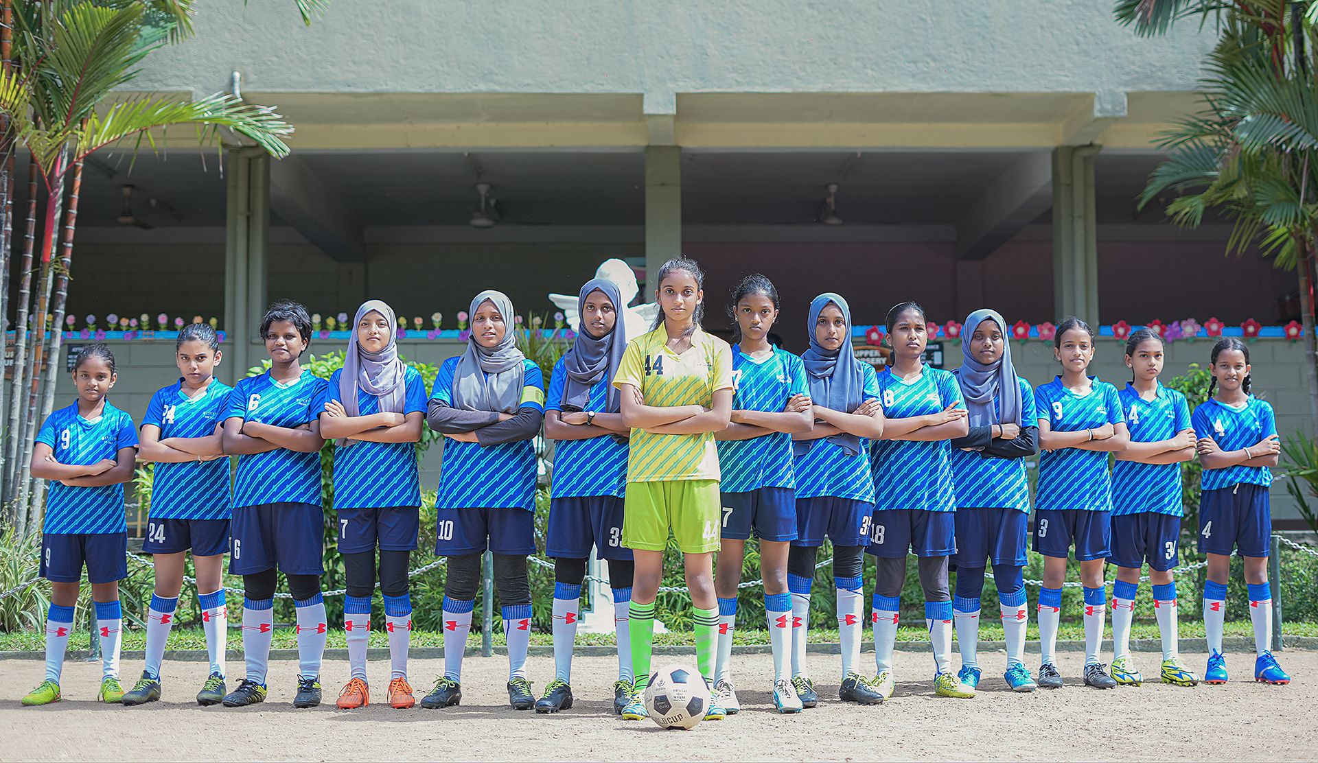 Determined girls soccer team in blue and green uniforms posing together.