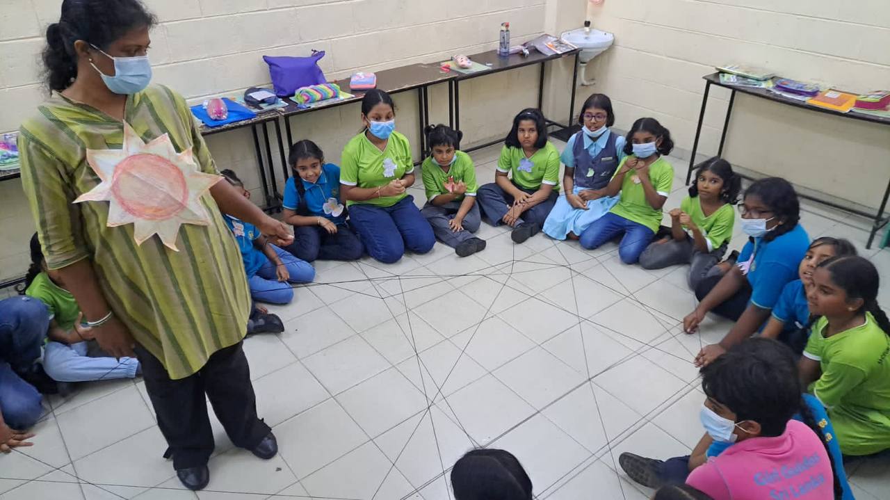Children and teacher perform a string activity in a classroom.