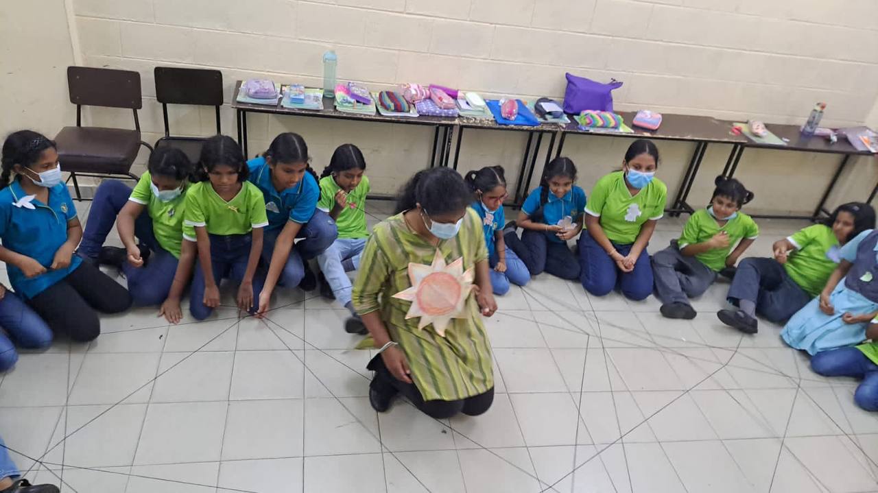 Children in blue and green shirts engage in storytelling with teacher holding sun cutout.