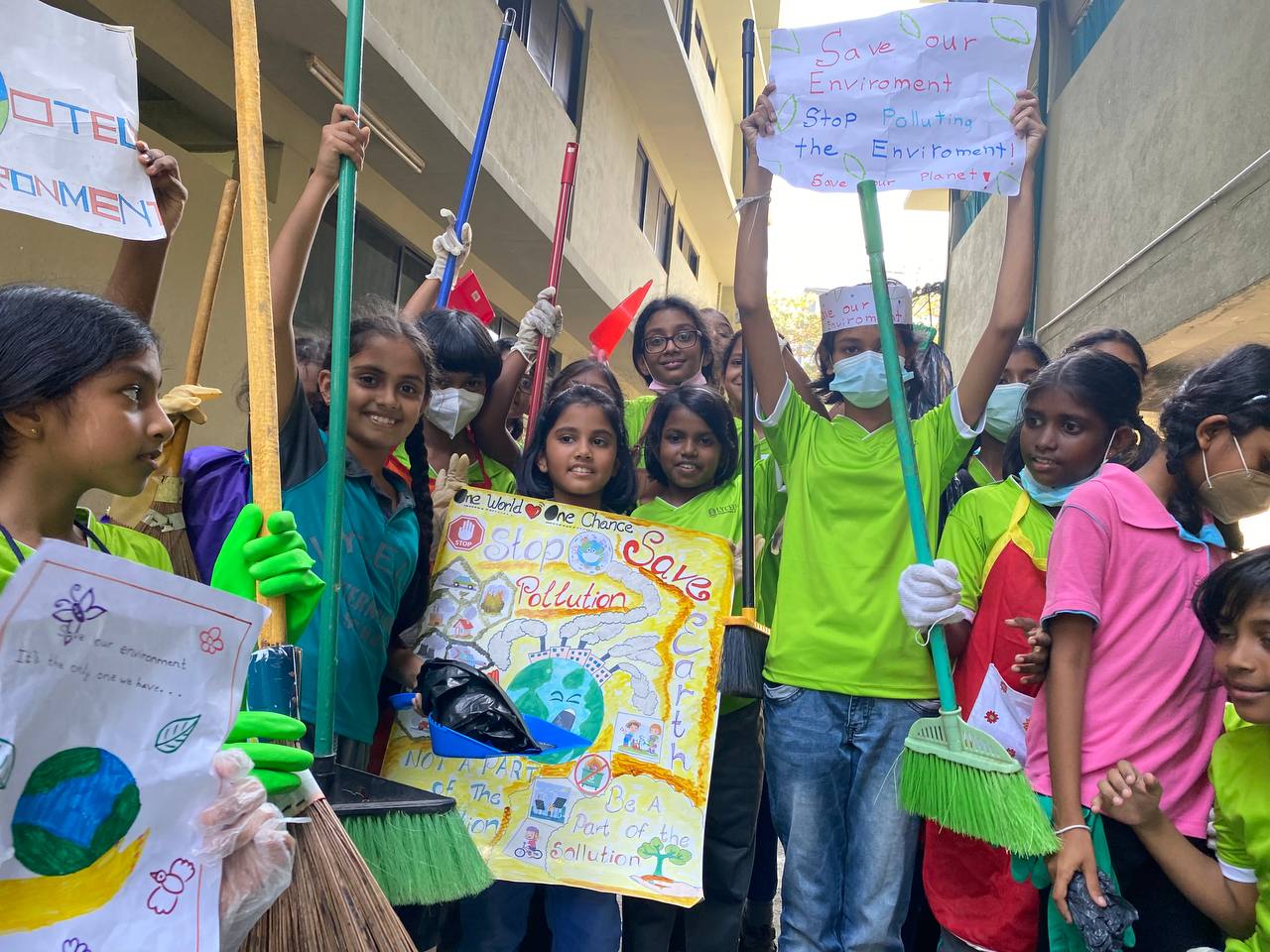 Children engaged in urban cleanup, holding brooms and posters promoting environmental awareness.