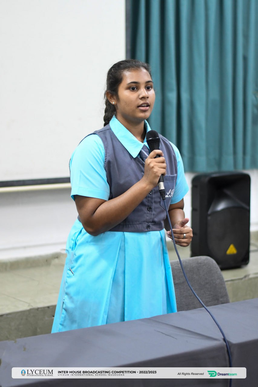 Teenage girl in school uniform speaking into a microphone at a formal event.