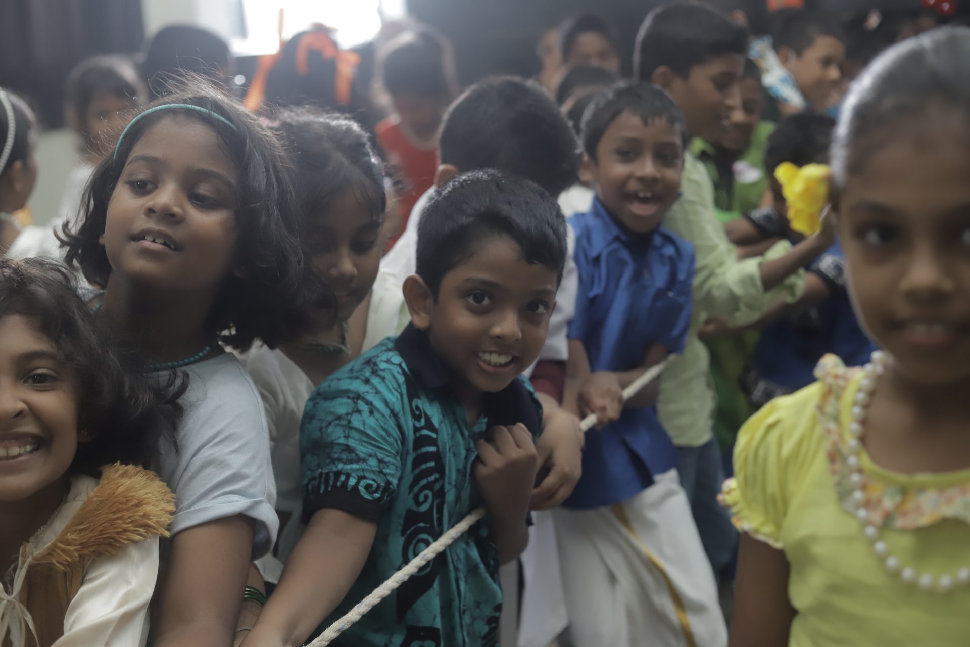 Children playing tug-of-war indoors, laughing and pulling a rope enthusiastically.