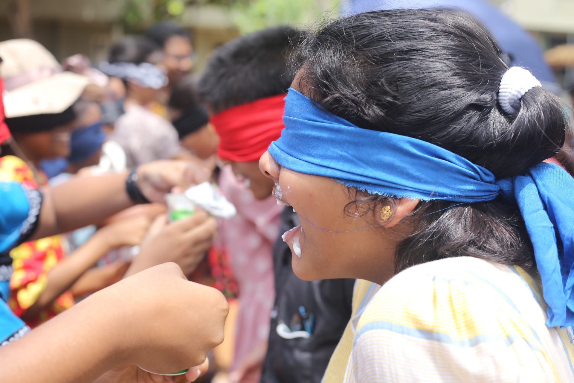 Children and adults in a lively outdoor blindfolded food challenge.