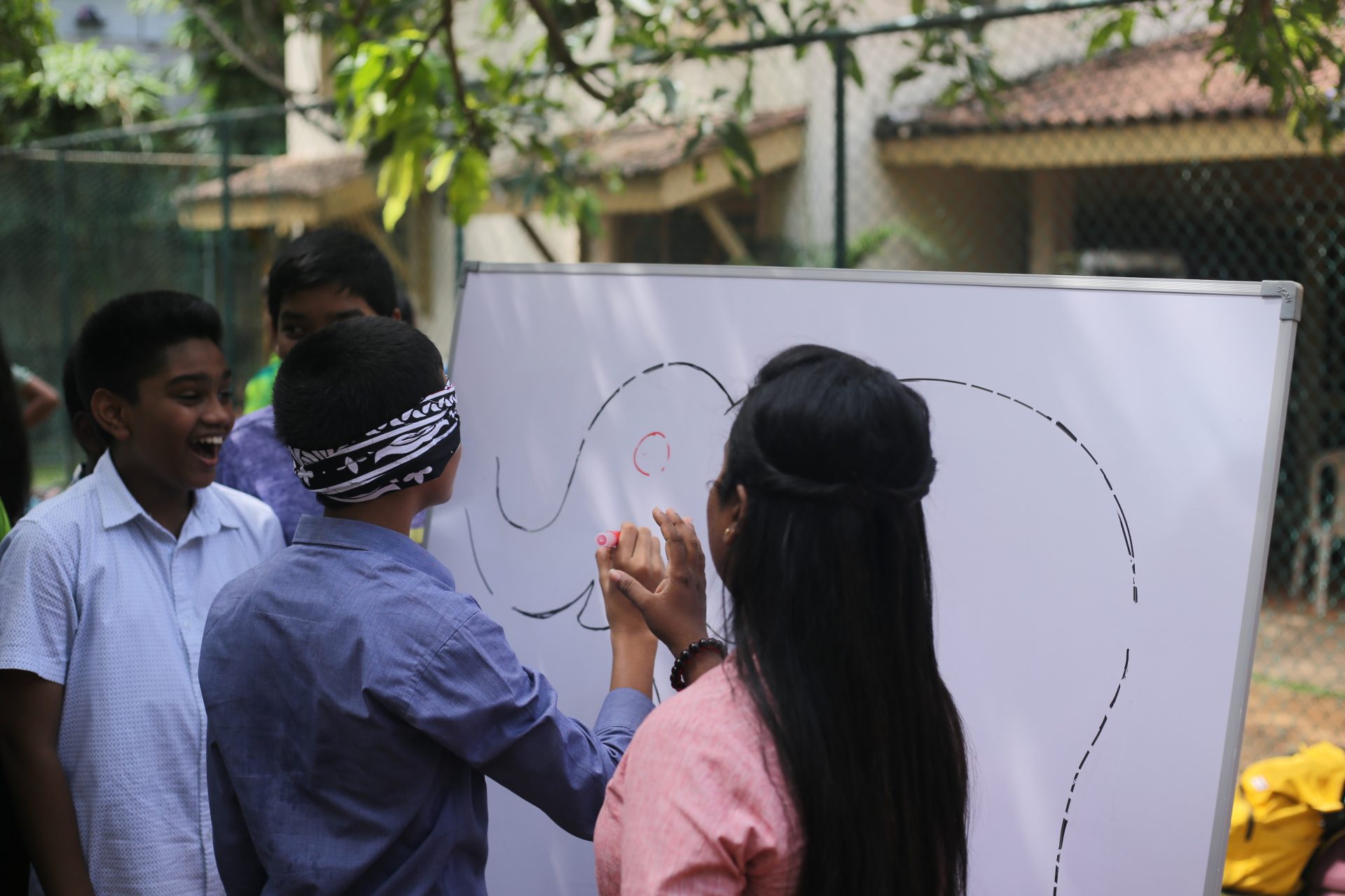 Blindfolded drawing game outdoors with friends, creating an elephant on a whiteboard.