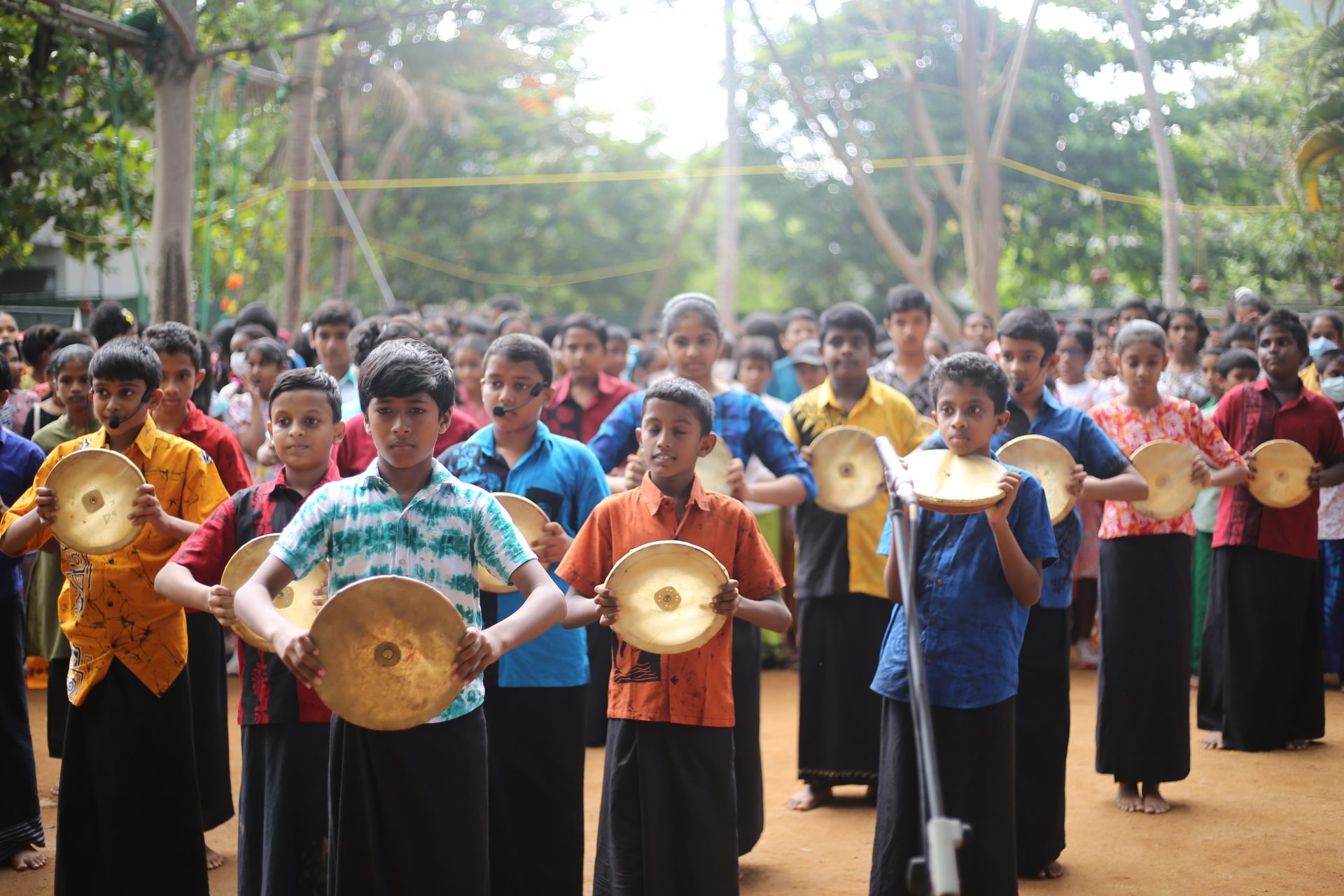 Children in colorful shirts performing with cymbals outdoors.