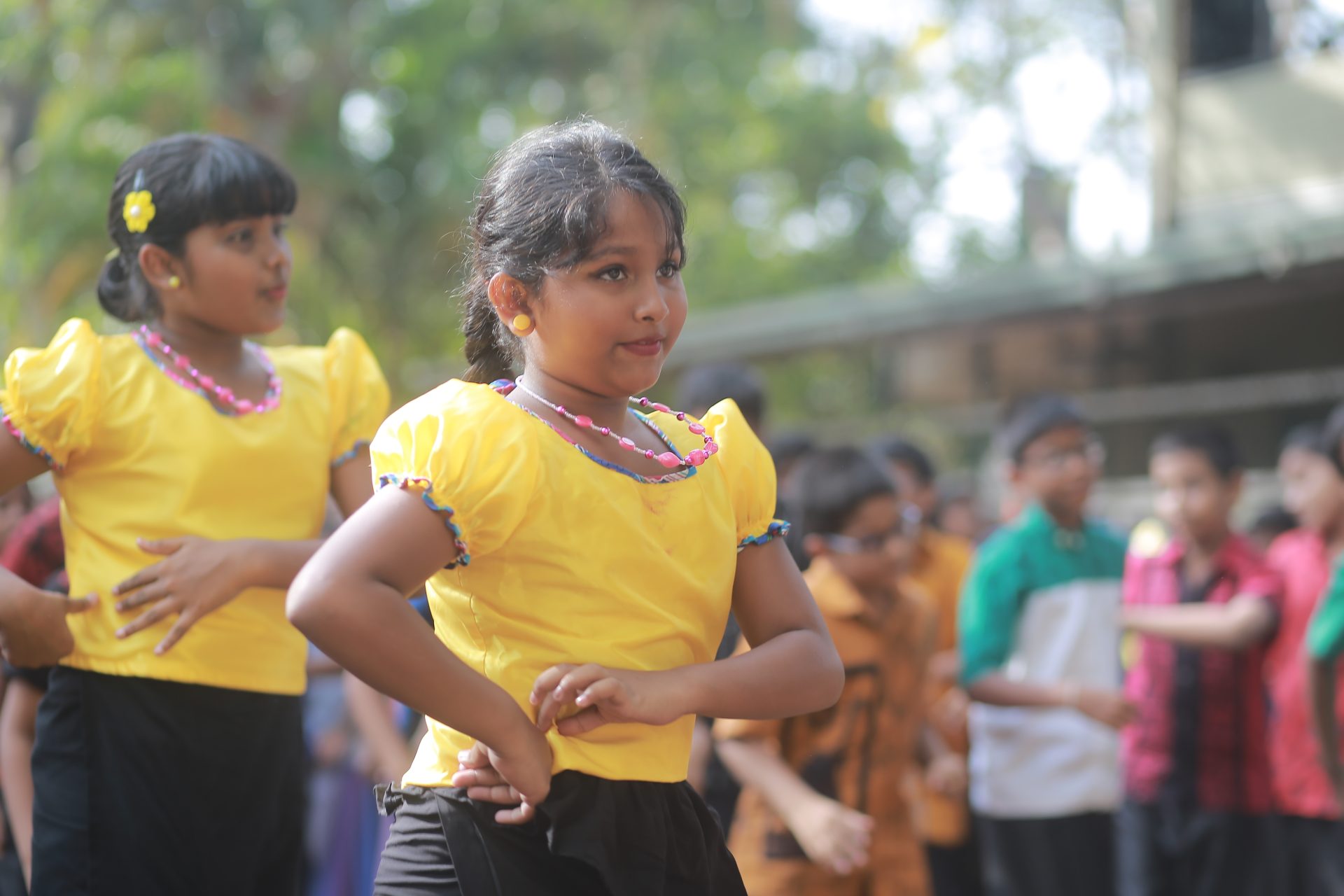 Children dancing outdoors in yellow tops, focused and enjoying the performance.